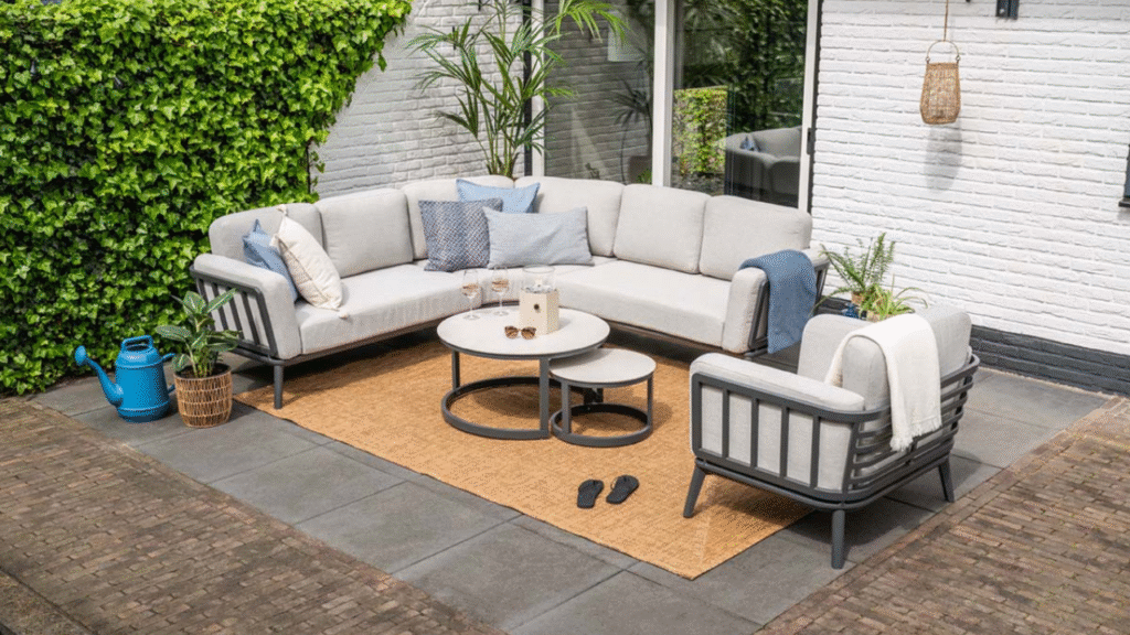 Lichtgrijze hoek loungeset met moderne ronde salontafels op strak terras met witte muur en groene klimop