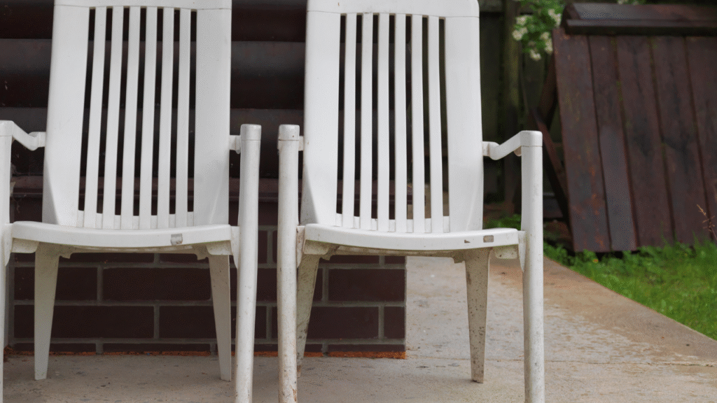 Twee verweerde witte kunststof tuinstoelen tegen een bakstenen muur op een betonnen terras